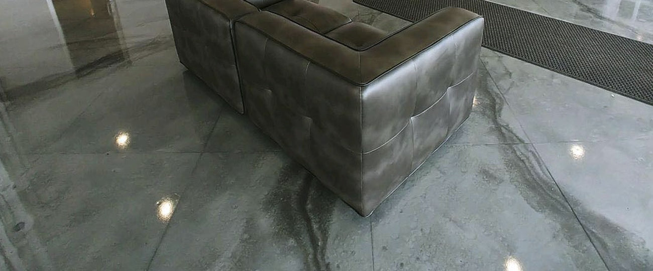 Finished silver and charcoal metallic epoxy floor in a showroom lounge, reflecting ceiling downlights
