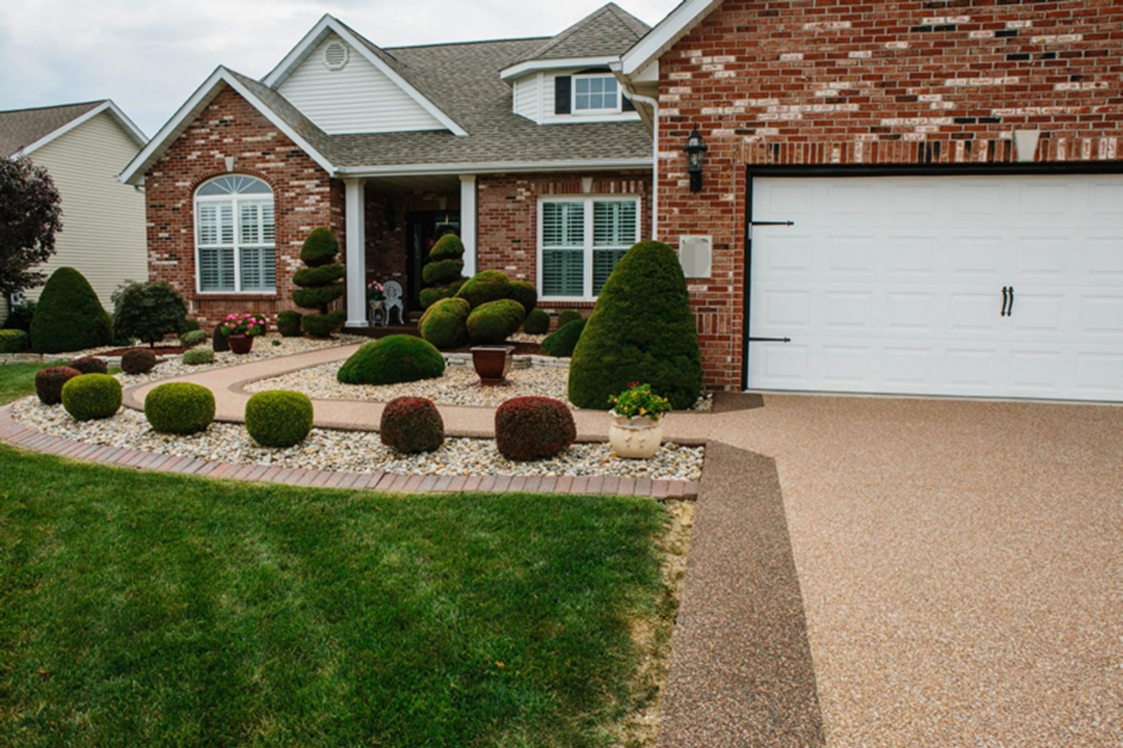 Front view of a brick house with a well-maintained lawn and a beautiful Stone Bond Epoxy driveway and walkway.